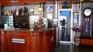 A reception area with a wooden counter, framed pictures, a clock, and a vase with flowers. - Jor Koo City Hotel (Ban Chang)