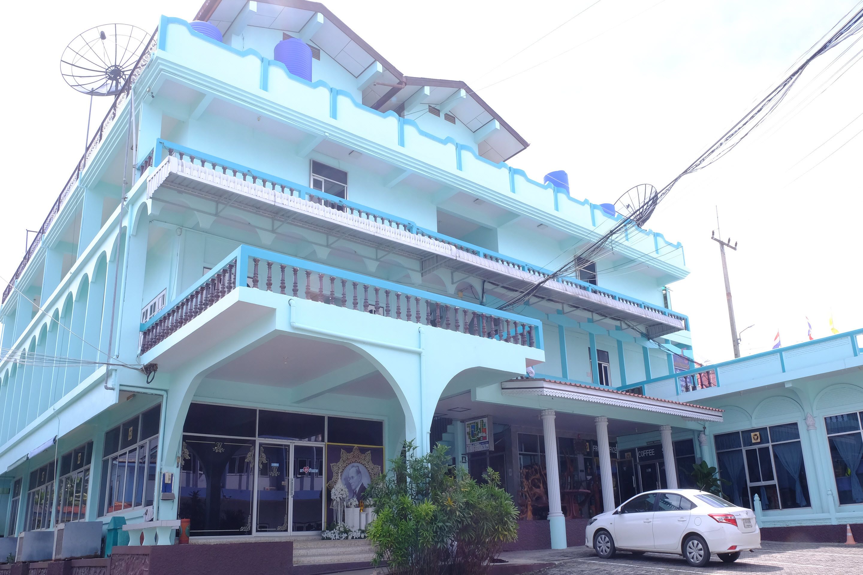 A multi-story building with a light blue facade, balconies, and a car parked in front.