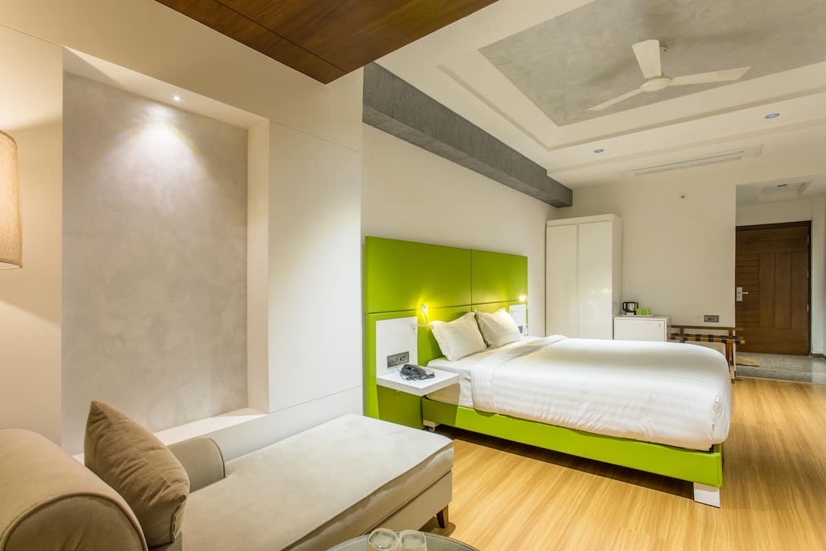 Una habitación de hotel moderna con una pared verde de acento, una cama grande, una mesita de noche con lámpara y suelo de madera.