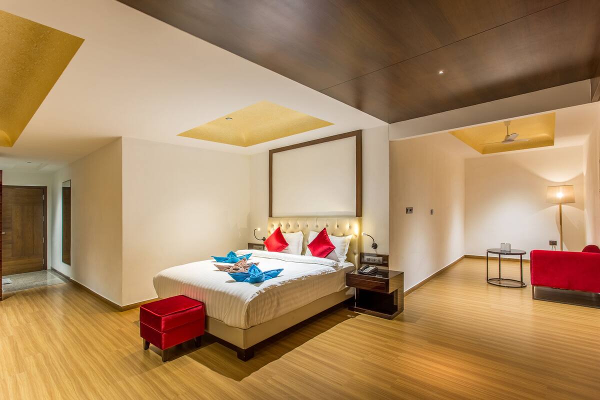 Una habitación de hotel moderna con una cama grande, un reposapiés rojo, una mesita de noche y un sillón rojo.