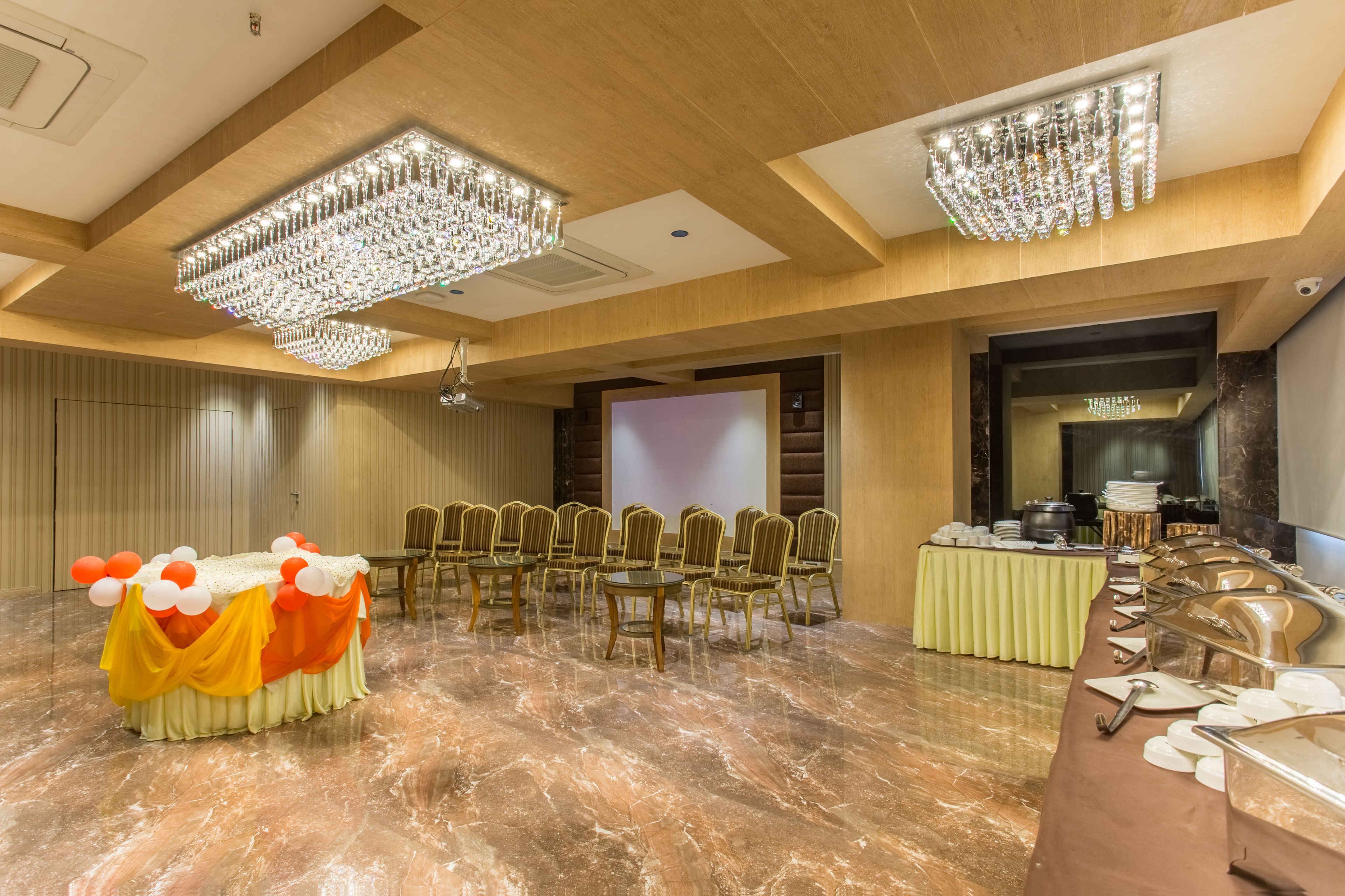 A banquet hall with a marble floor, rows of chairs, a buffet table, and chandeliers.