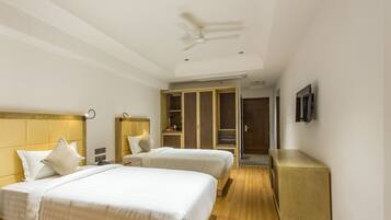 Quarto de hotel com duas camas, ventoinha no teto, guarda-roupa, mesa de cabeceira e televisão fixada na parede.