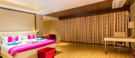 A modern hotel room with a large bed, a desk, and a large window with curtains.