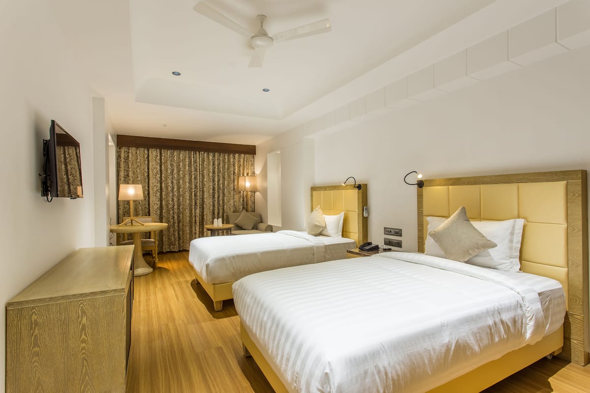 Habitación de hotel con dos camas, un escritorio, una silla, un televisor y un ventilador de techo.