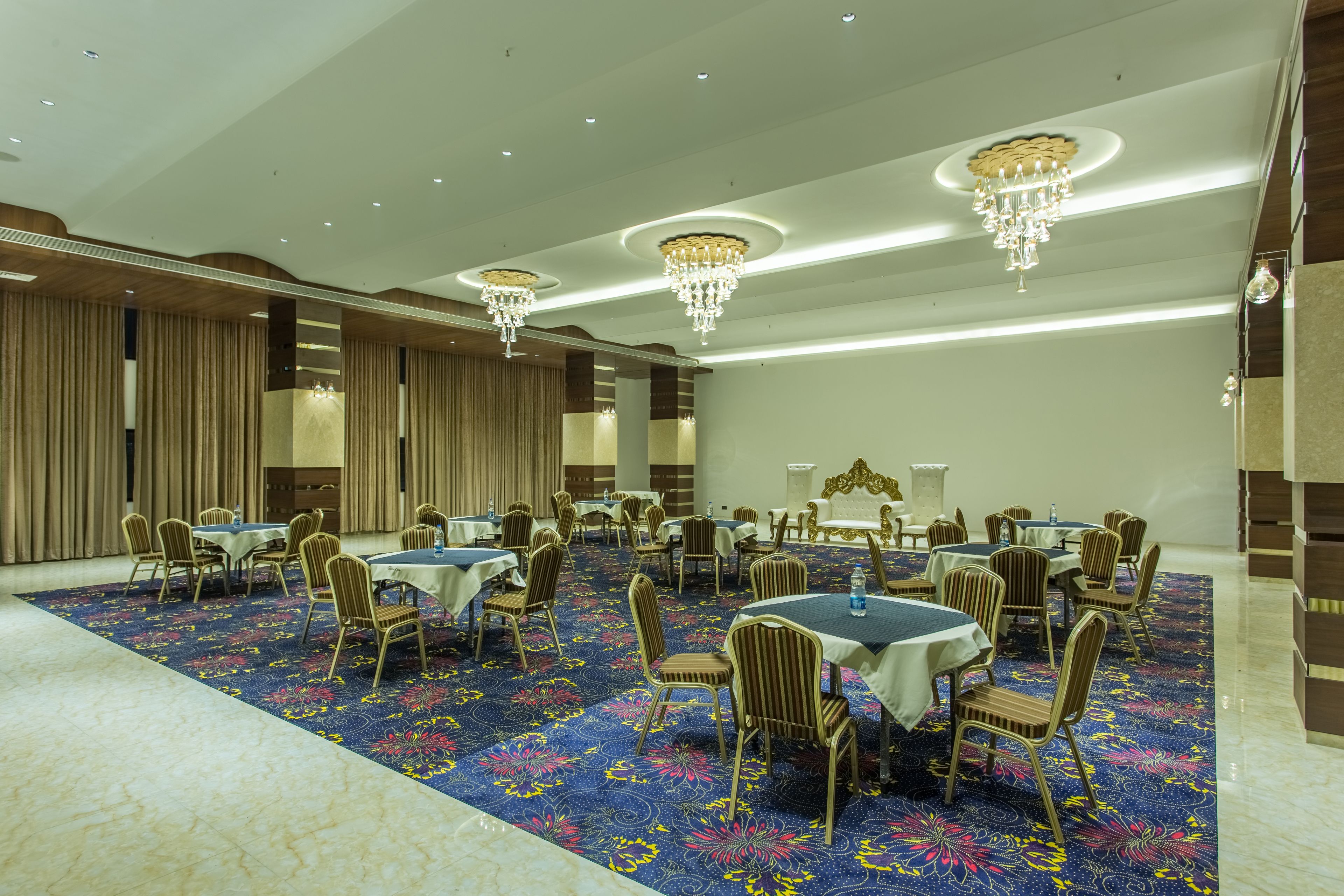 A banquet hall with round tables and chairs, chandeliers, and a patterned carpet.