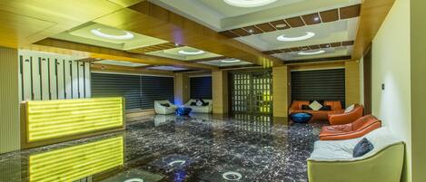 Un moderno vestíbulo con piso de mármol, zonas de estar y techo de madera con iluminación circular.