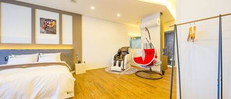A modern hotel room with a wooden floor, a bed with white bedding, a red and white chair, and a large mirror.