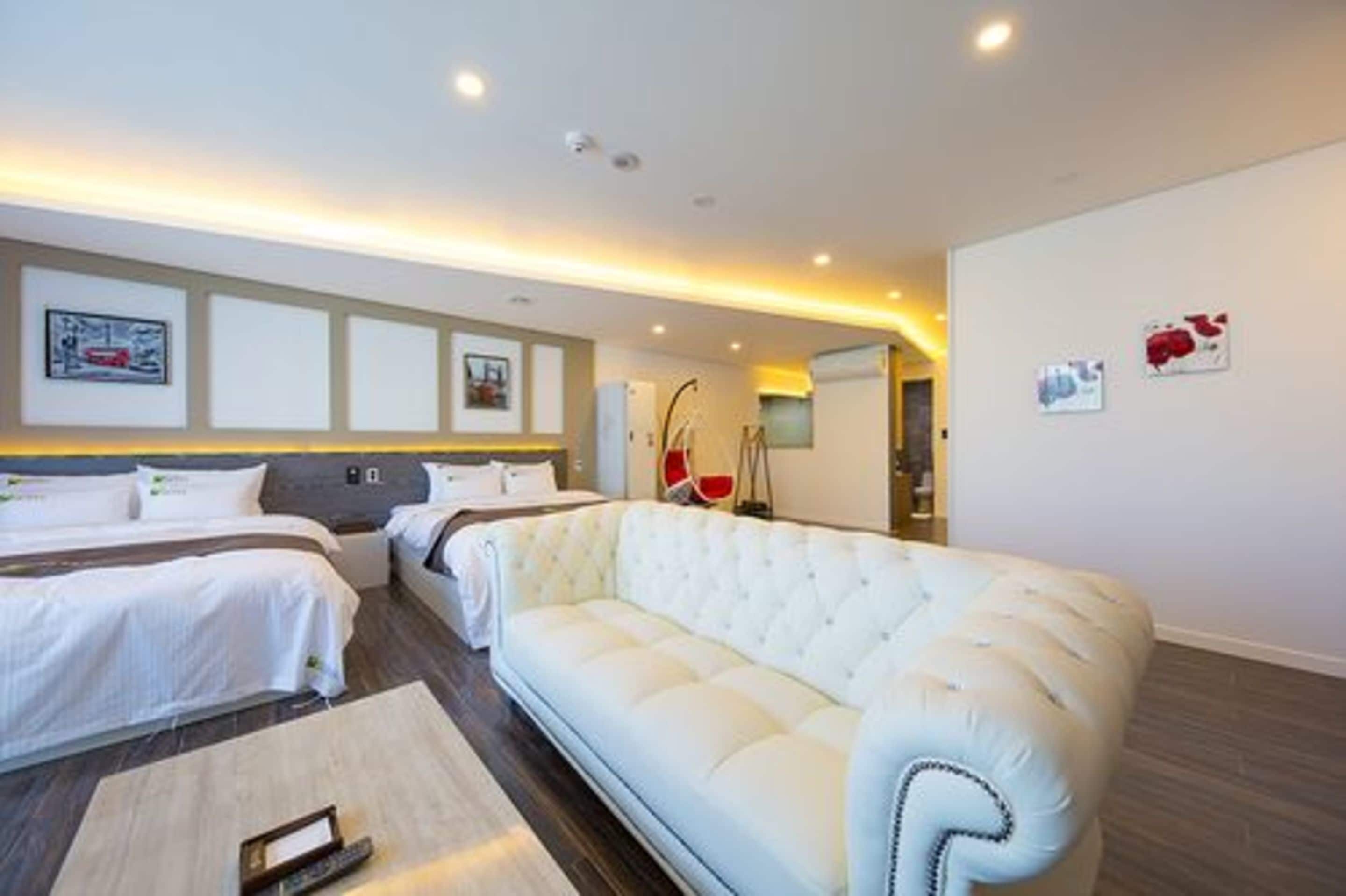 A hotel room with two beds, a white sofa, and a small table.