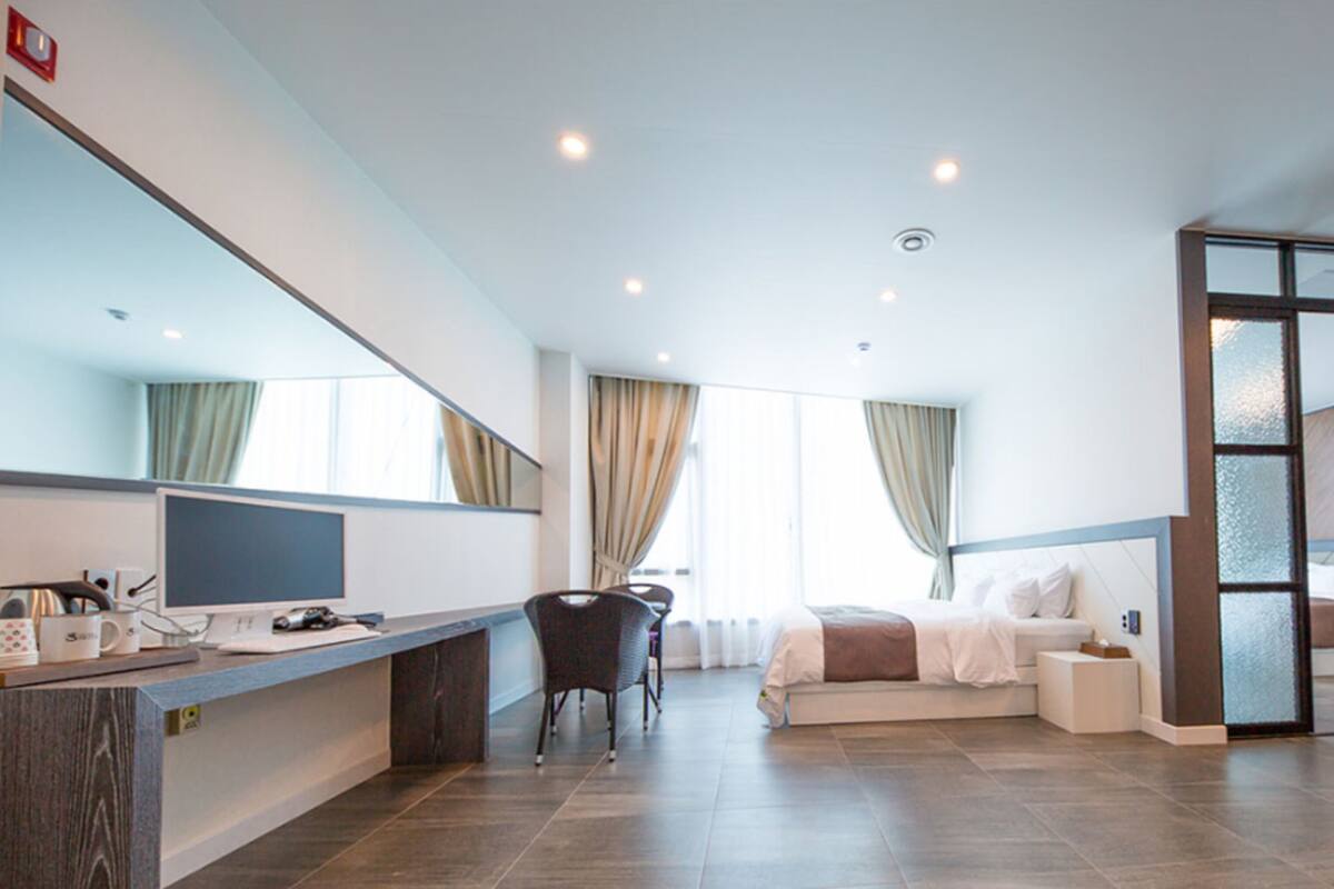 Ein modernes Hotelzimmer mit Schreibtisch, Bett, Sitzecke und großem Fenster.