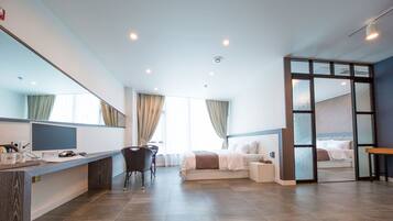 A modern hotel room with a desk, a bed, a seating area, and a large window.