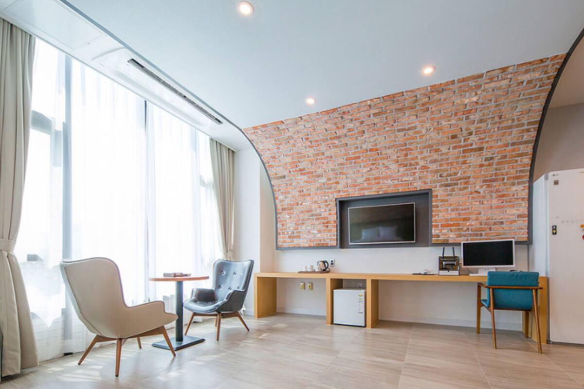 Ein modernes Wohnzimmer mit Ziegelwand, Flachbildfernseher, Schreibtisch mit Computer und einer Sitzecke mit zwei Sesseln.