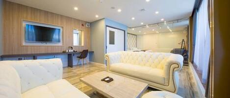 A modern living room with a large flat-screen TV, a white sofa, a coffee table, and a wooden accent wall.
