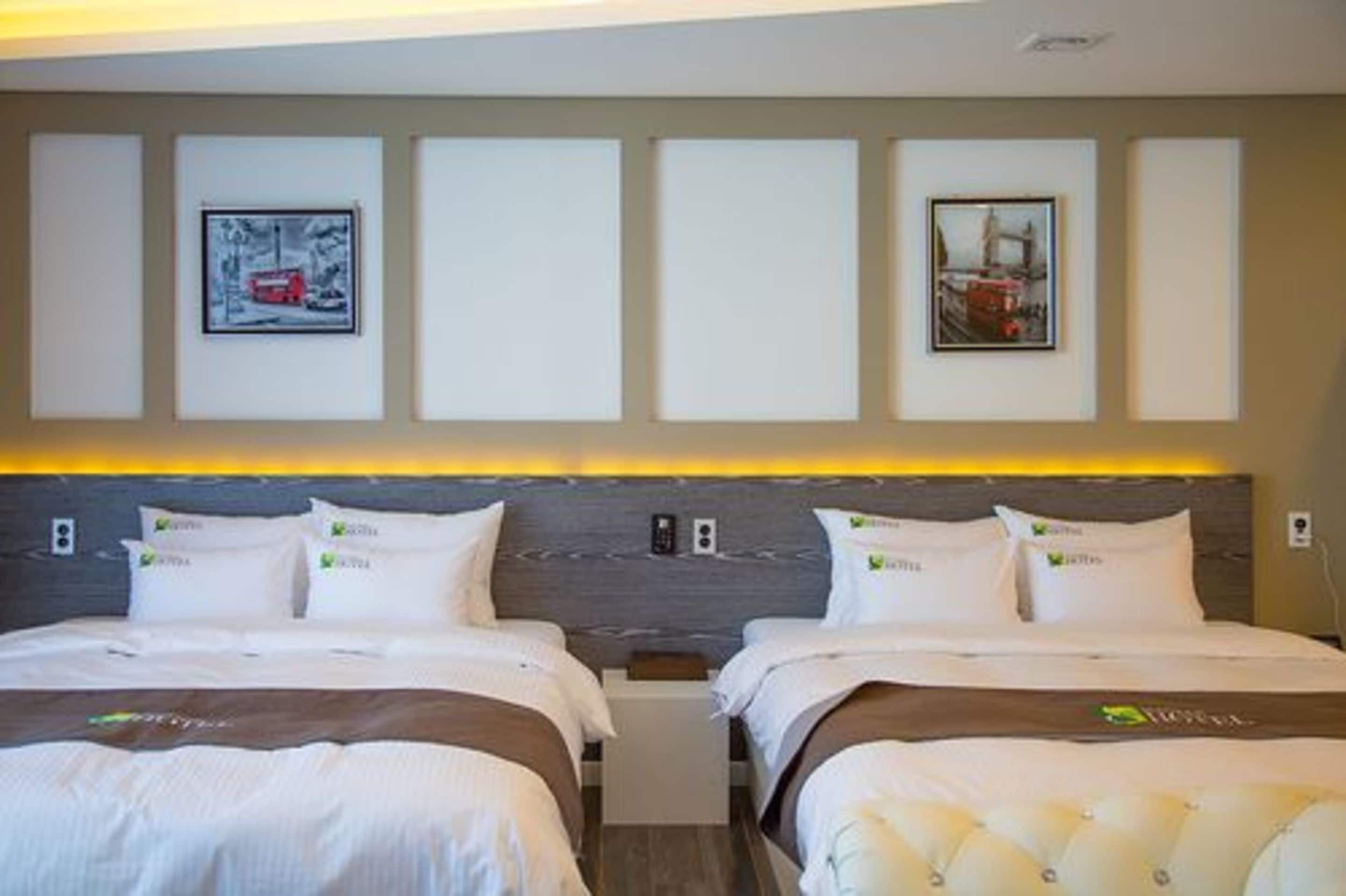 A hotel room with two beds, a headboard with built-in lighting, and framed pictures on the wall.