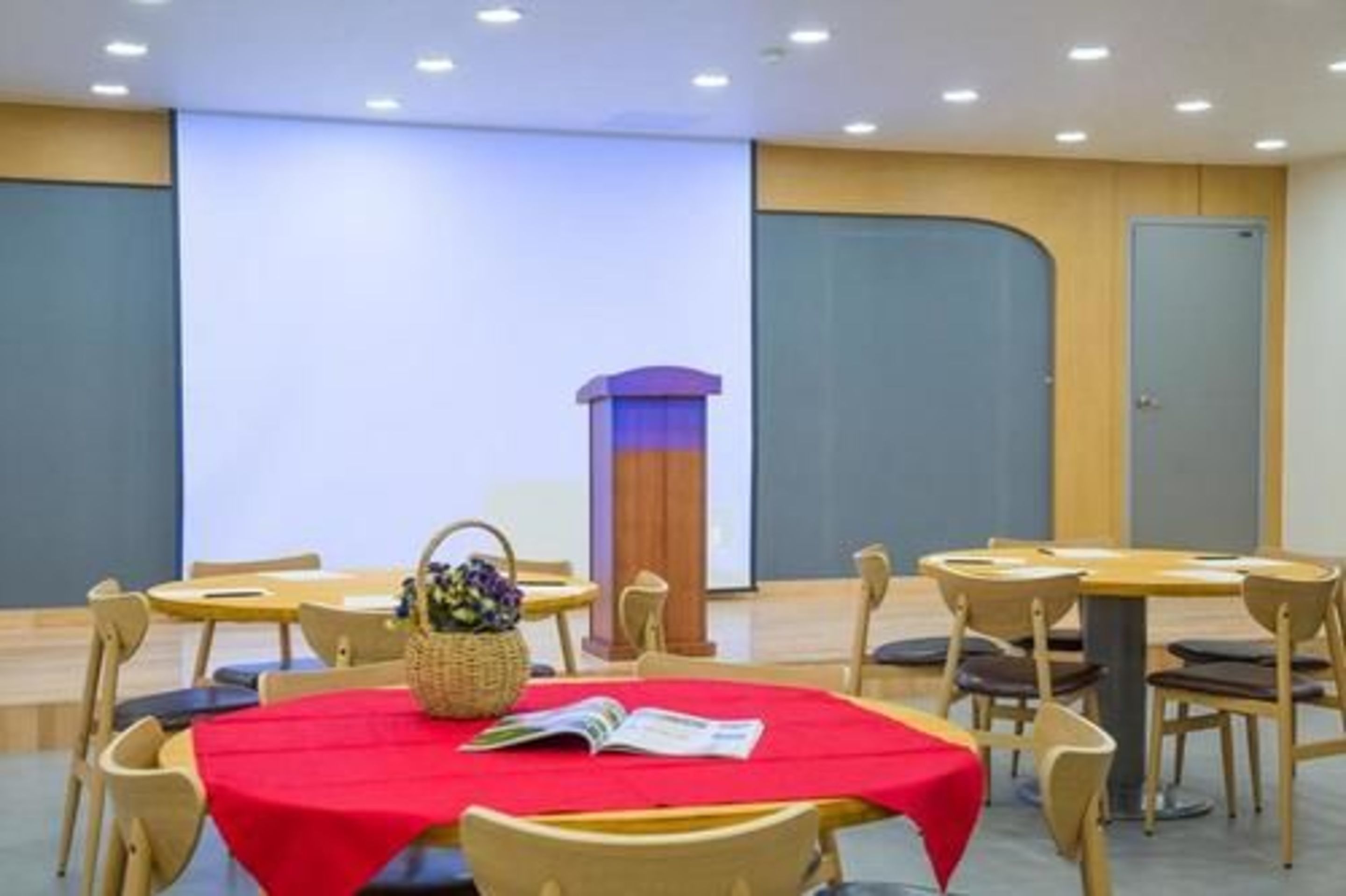 A conference room with round tables, chairs, a podium, and a large screen.
