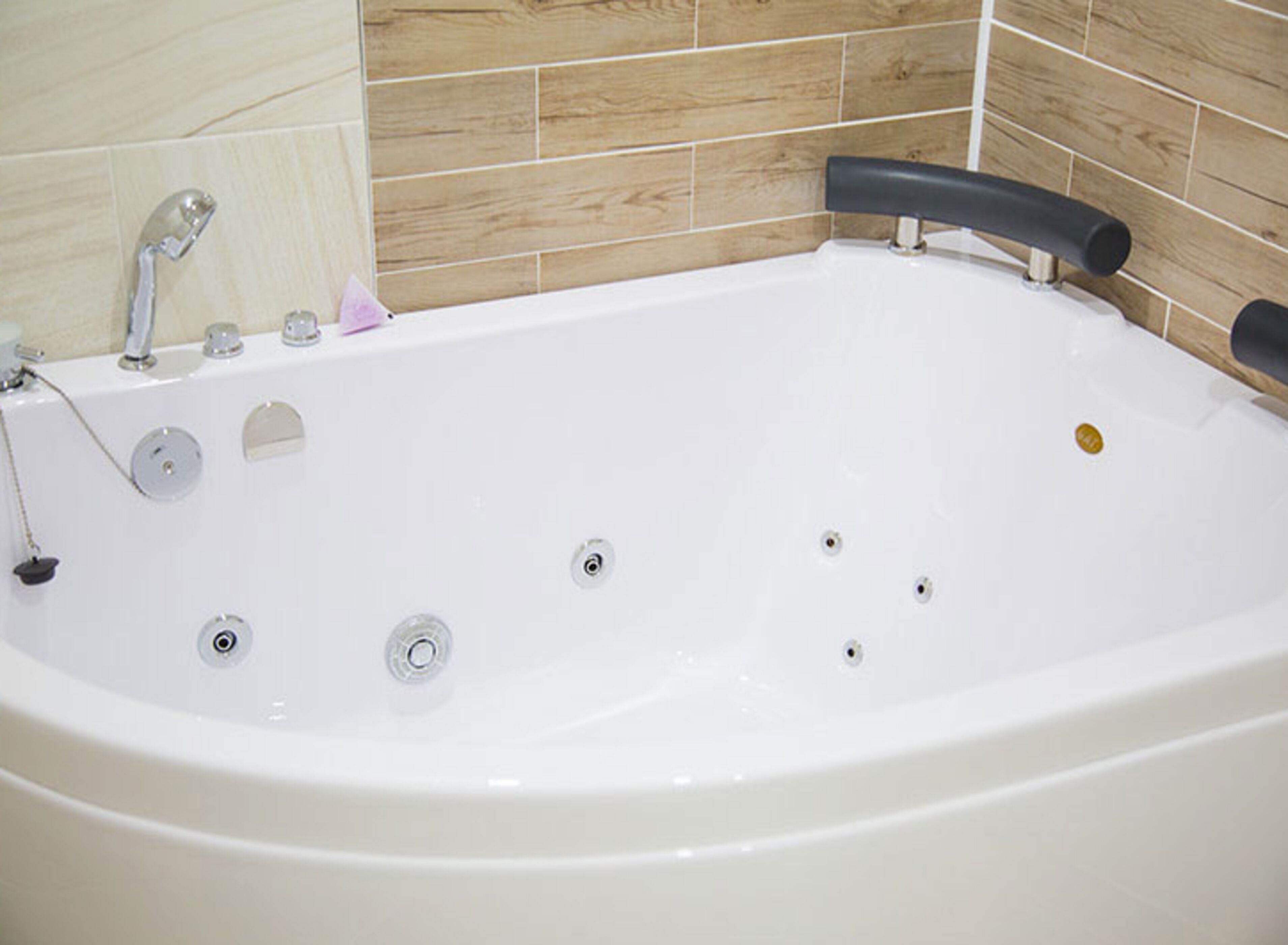 A white bathtub with a black faucet handle, a handheld showerhead, and a small bottle of shampoo.