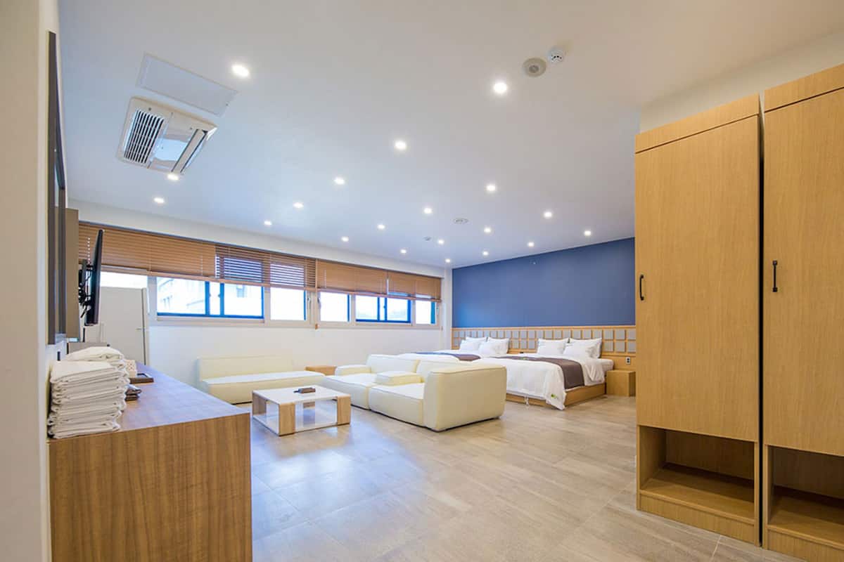 Ein modernes Hotelzimmer mit einem großen Bett, einer Sitzecke mit einer Couch und Sesseln, einem Holzschrank und einem Schreibtisch mit Stuhl.