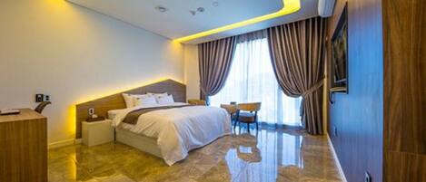 A modern hotel room with a large bed, a bedside table, a desk, and a chair.