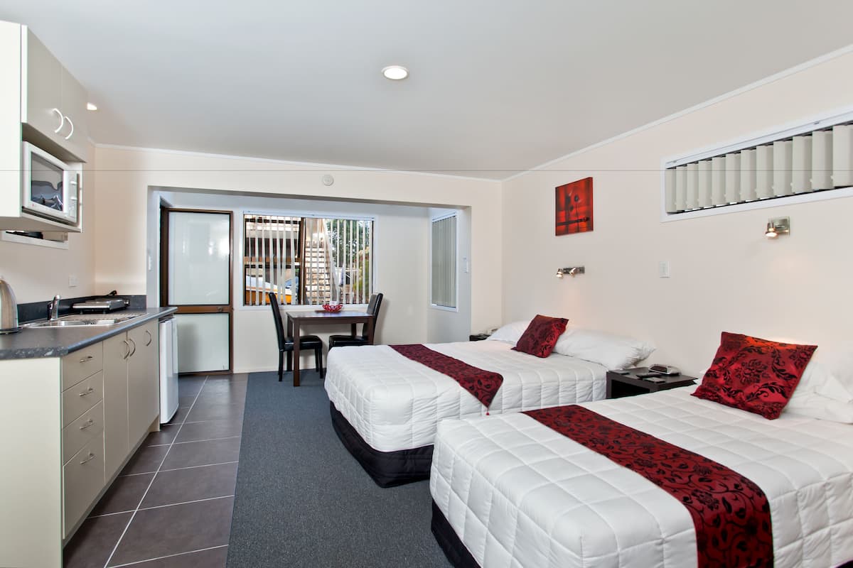 A hotel room with two beds, a kitchenette, a dining area, and a view of the outside.