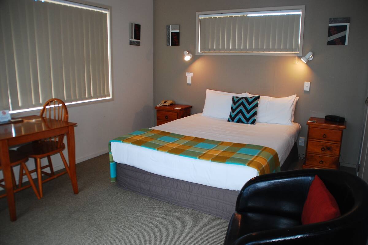 A hotel room with a bed, a desk, a chair, and a nightstand.
