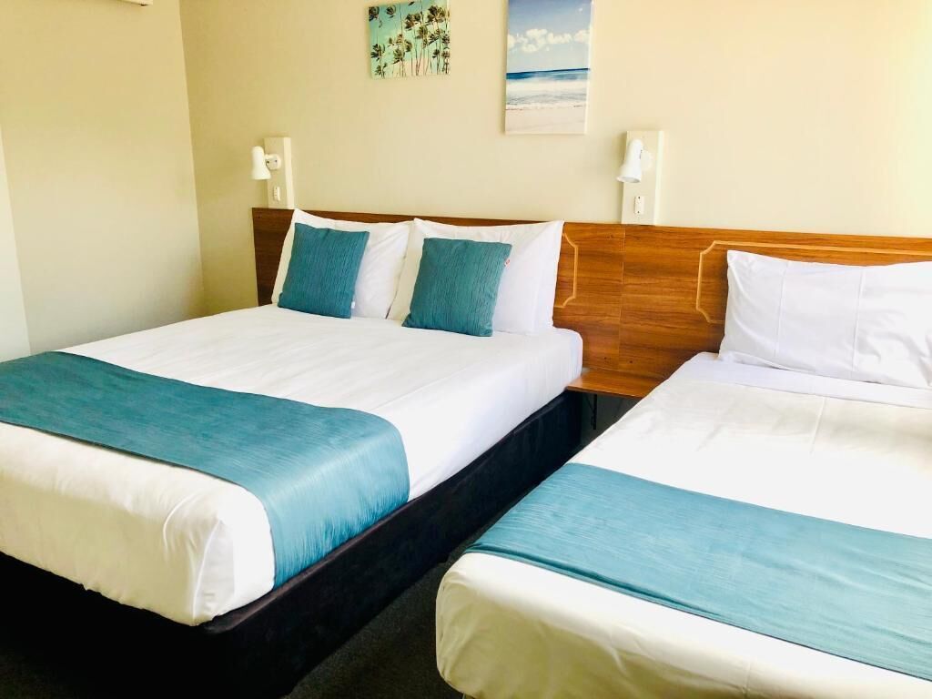 Two twin beds with wooden headboards, white bedding, and teal throw pillows.