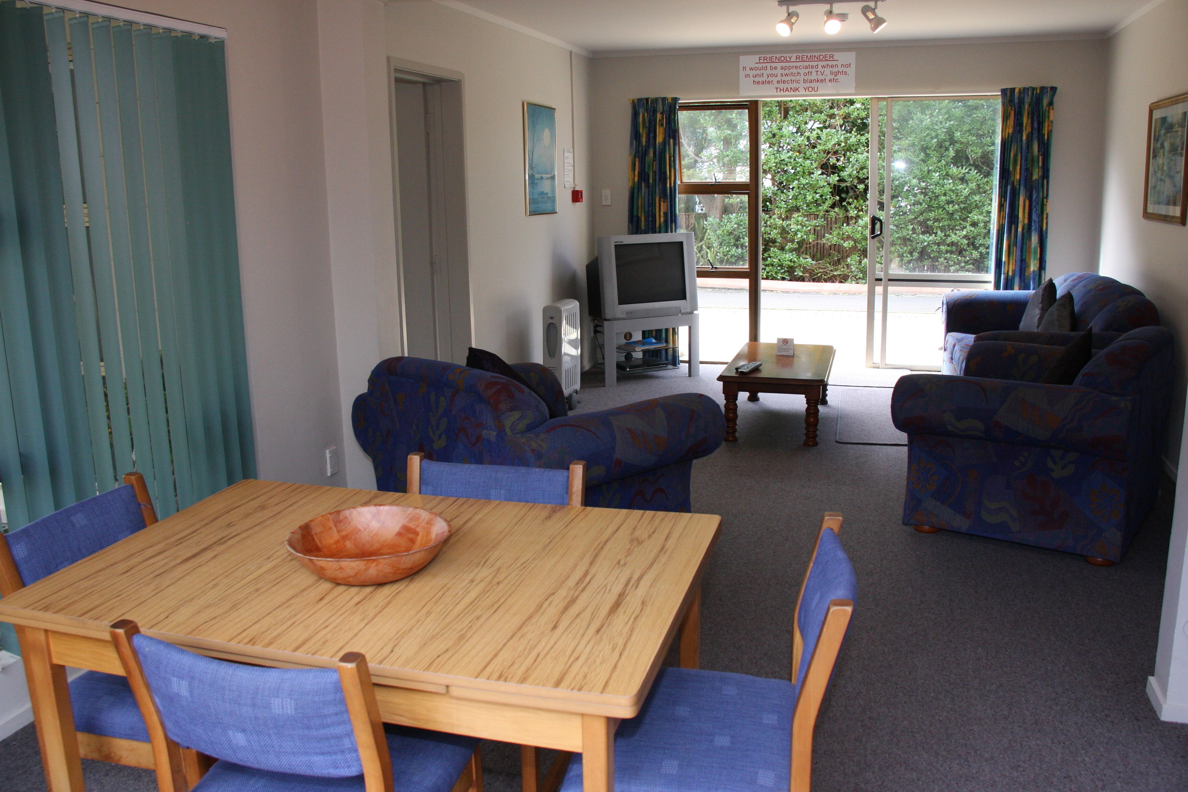 A room with a wooden table and blue chairs, a blue sofa, a television, and a window with curtains.