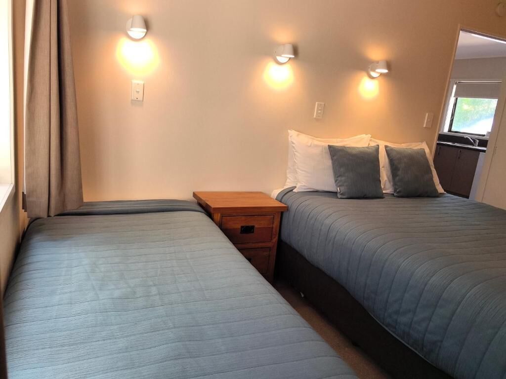 A hotel room with two beds, a nightstand, and wall-mounted lights.