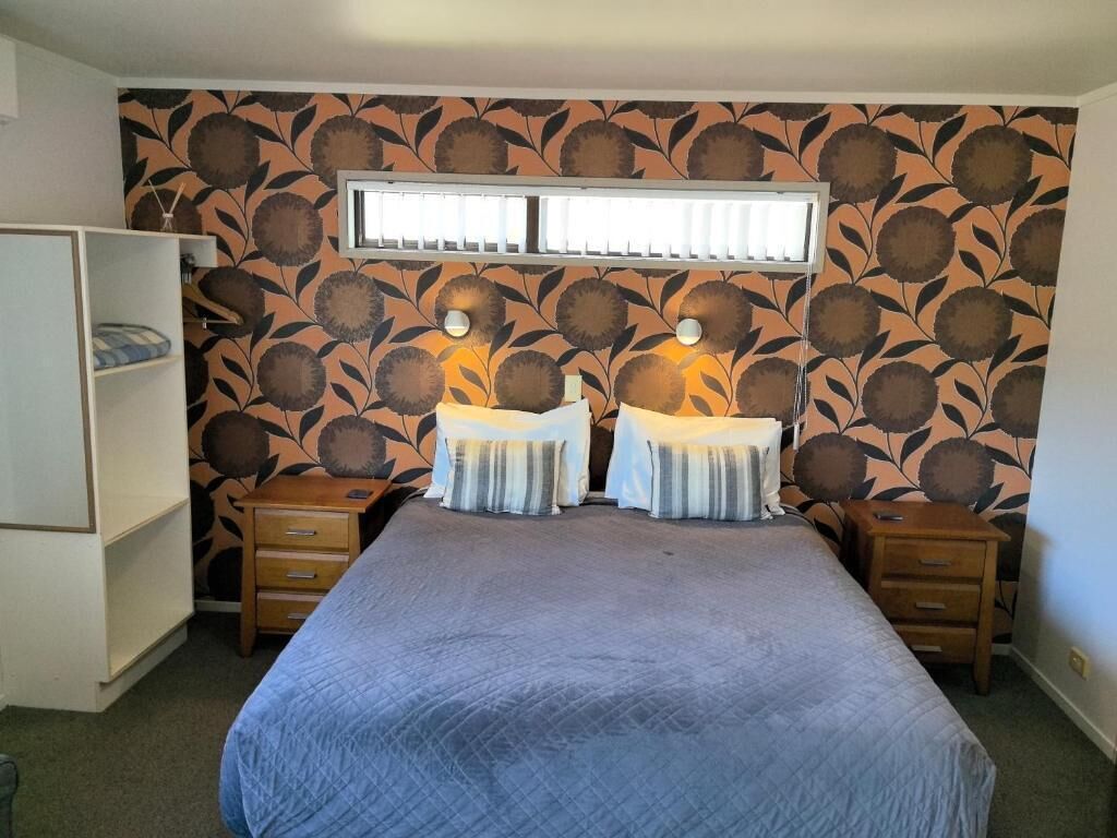A bedroom with a bed, two bedside tables, a wardrobe, and a window with blinds.