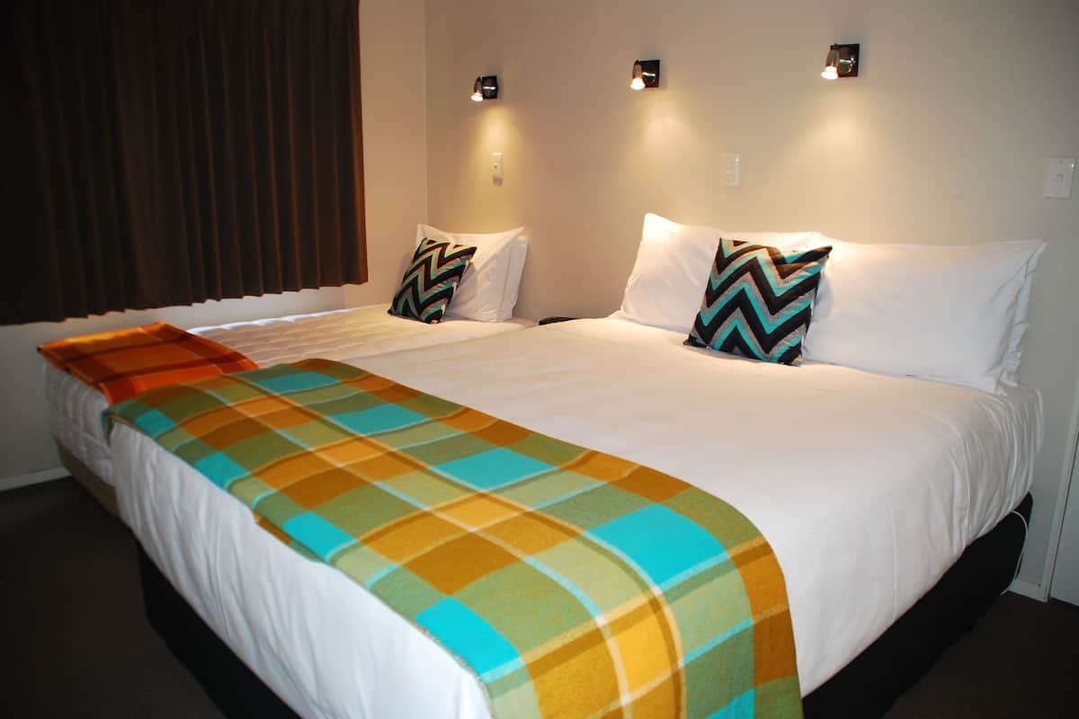 A hotel room with a large bed, two bedside tables, a window with curtains, and a wall-mounted light fixture.