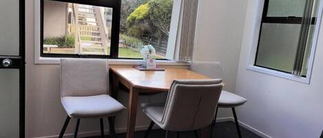 Un comedor con una mesa y cuatro sillas, una ventana que ofrece vistas a un edificio residencial y una puerta con pomo.