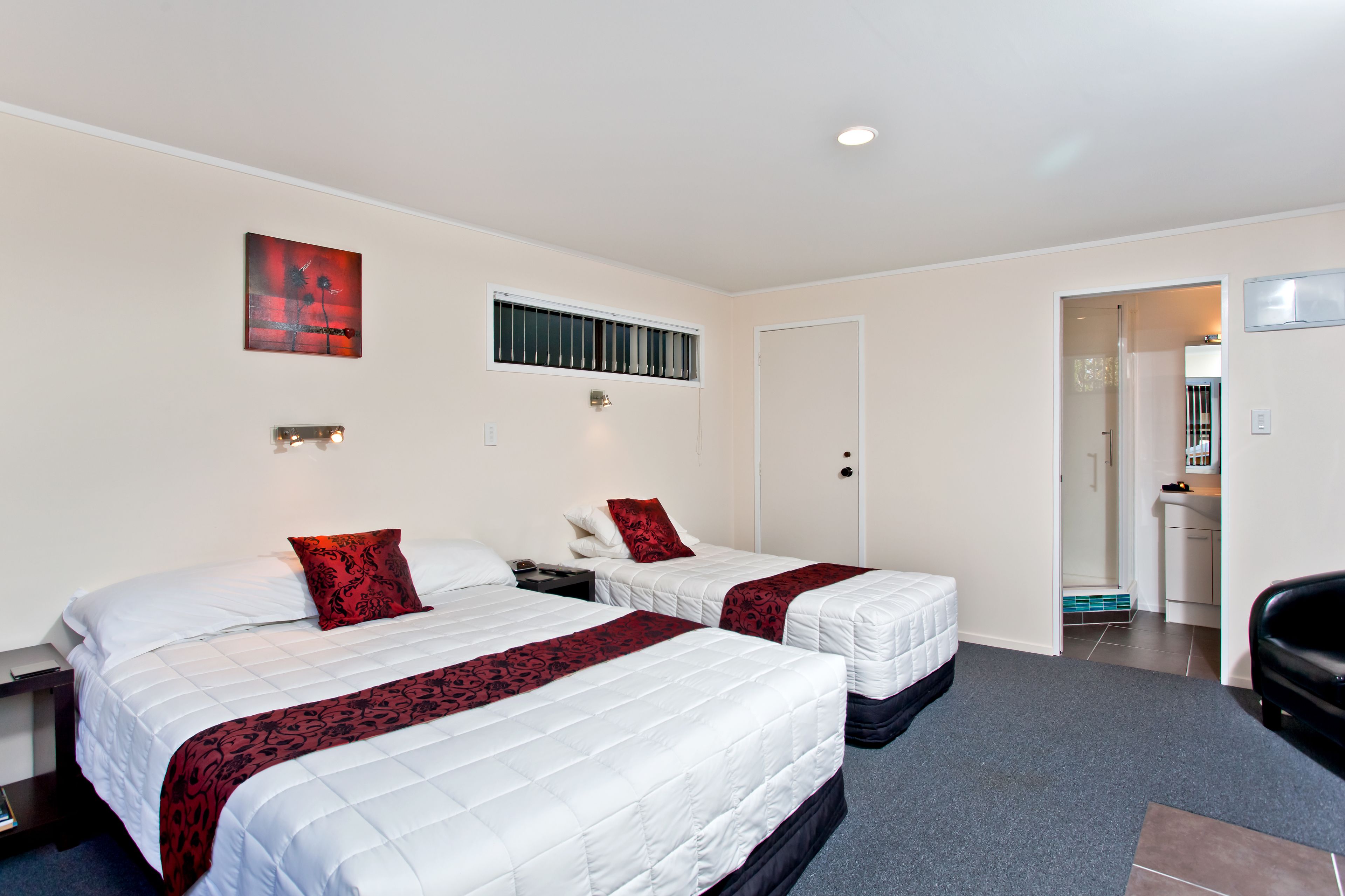 A hotel room with two beds, a small kitchenette, and a bathroom visible through an open door.