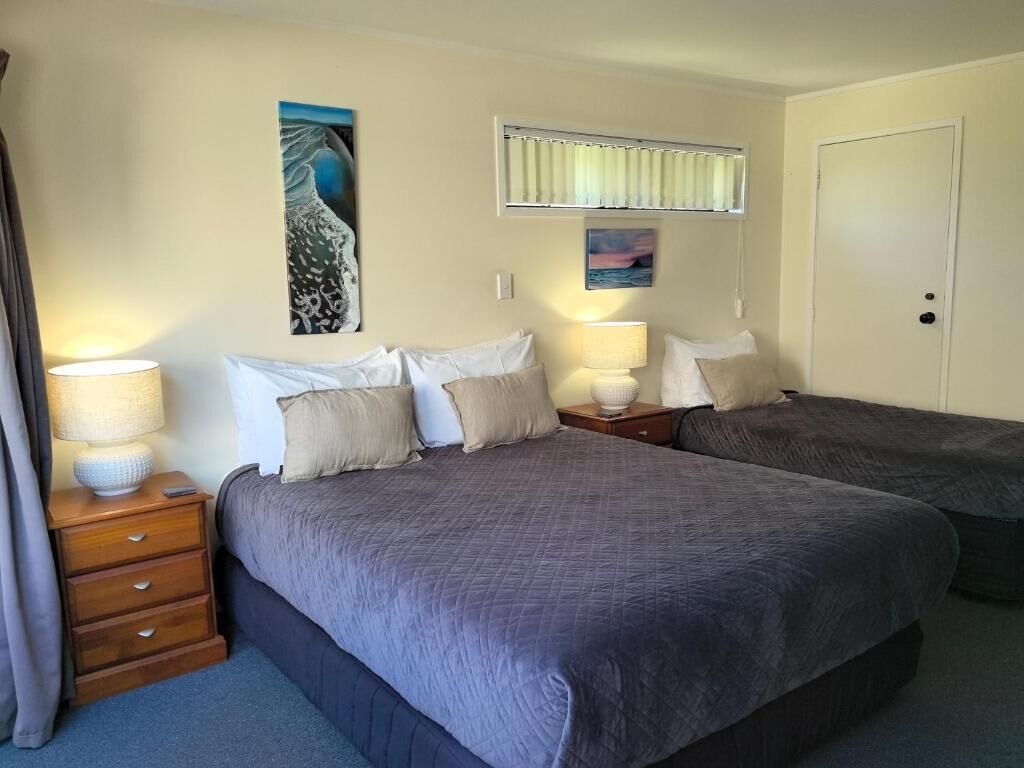 A hotel room with two beds, a nightstand with lamps, and artwork on the walls.