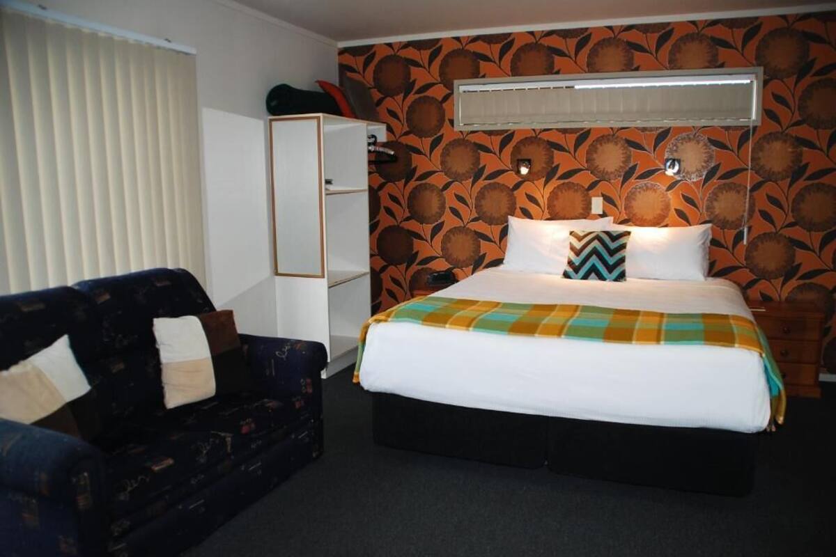 A hotel room with a bed, a sofa, a wardrobe, and a patterned wall.