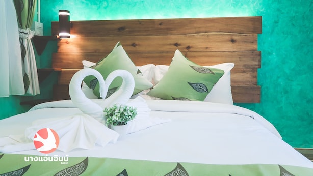A neatly made bed with a wooden headboard, green patterned pillows, and a swan-shaped towel arrangement.