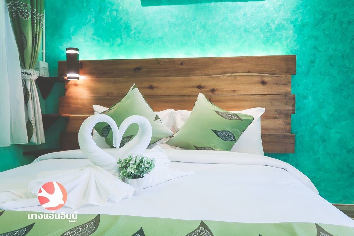 A neatly made bed with a wooden headboard, green patterned pillows, and a swan-shaped towel arrangement.