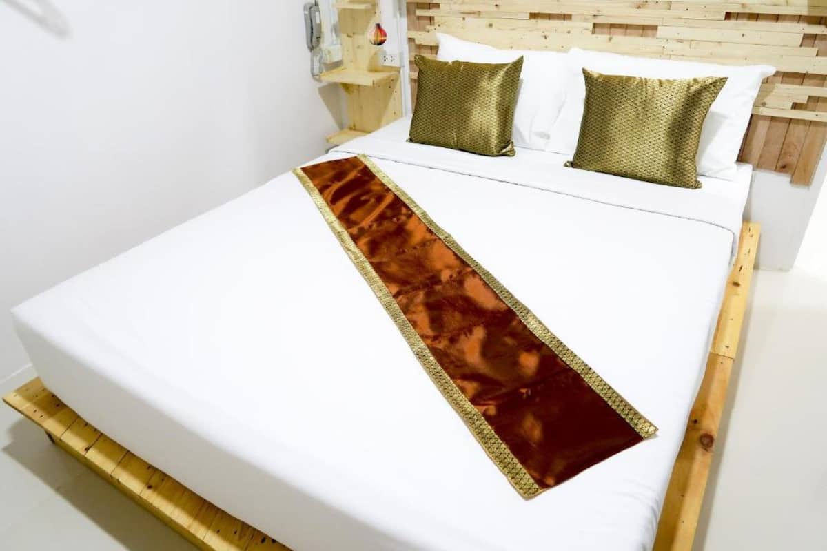 Un lit bien fait, avec un matelas blanc, un chemin de lit décoratif aux tons marron et or, et deux coussins verts.