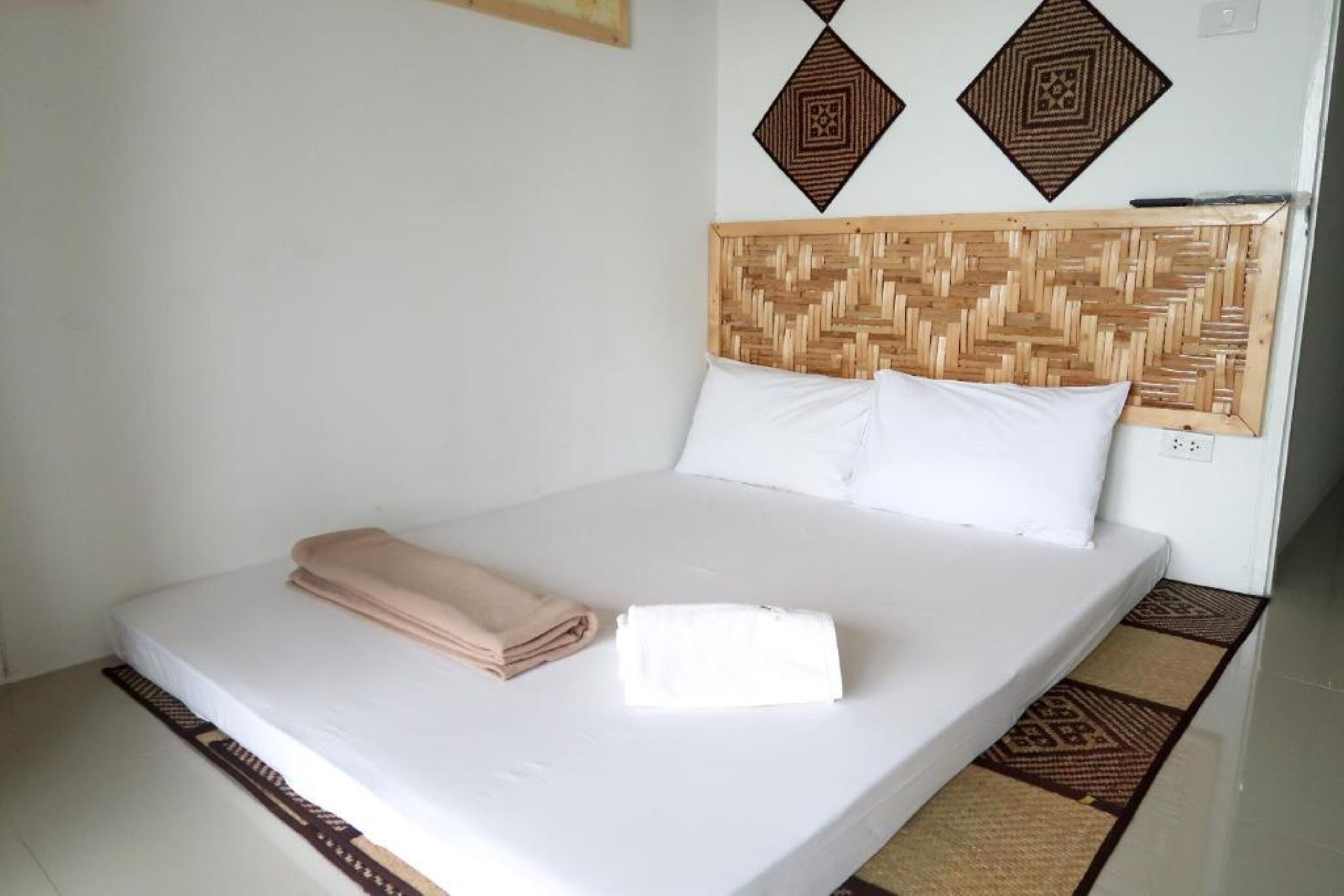 A neatly made bed with a woven headboard, white bedding, and a folded beige towel.