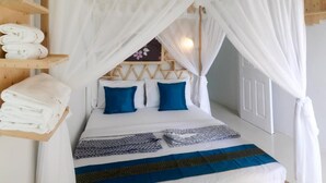 A neatly made bed with a canopy, a shelf with folded towels, and a patterned blanket. - Baan URT Suratthani Airport Hotel (Phunphin)