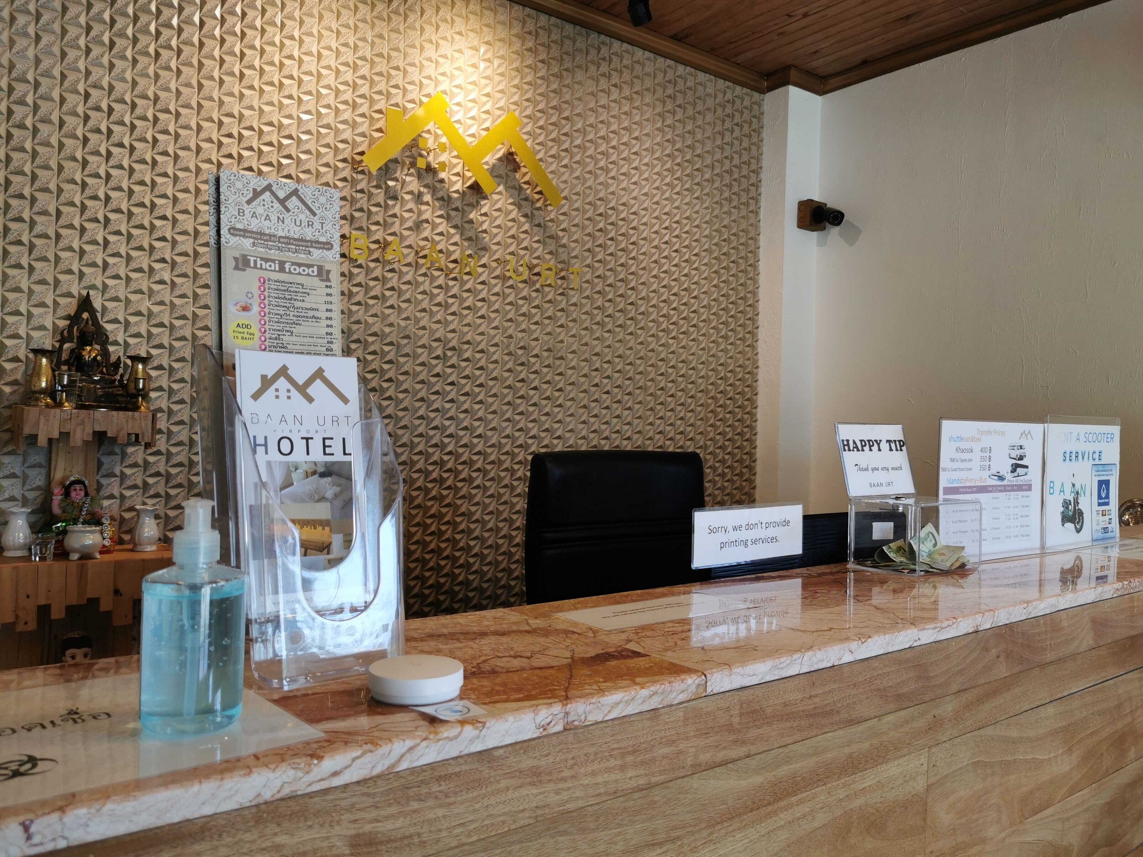 A hotel reception desk with a textured wall, a Buddha statue, and various informational signs.