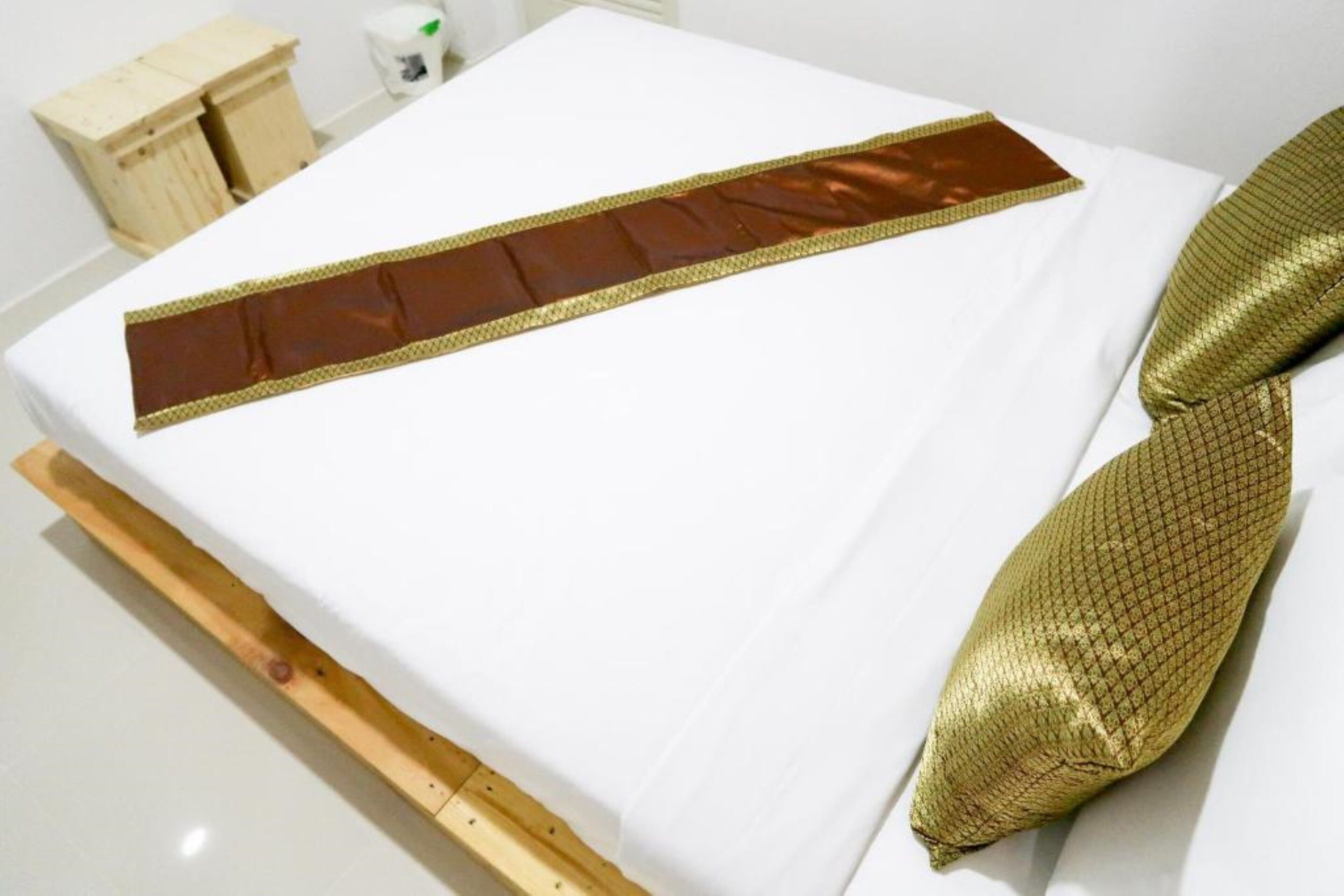Una cama con sábana blanca y una franja decorativa marrón.
