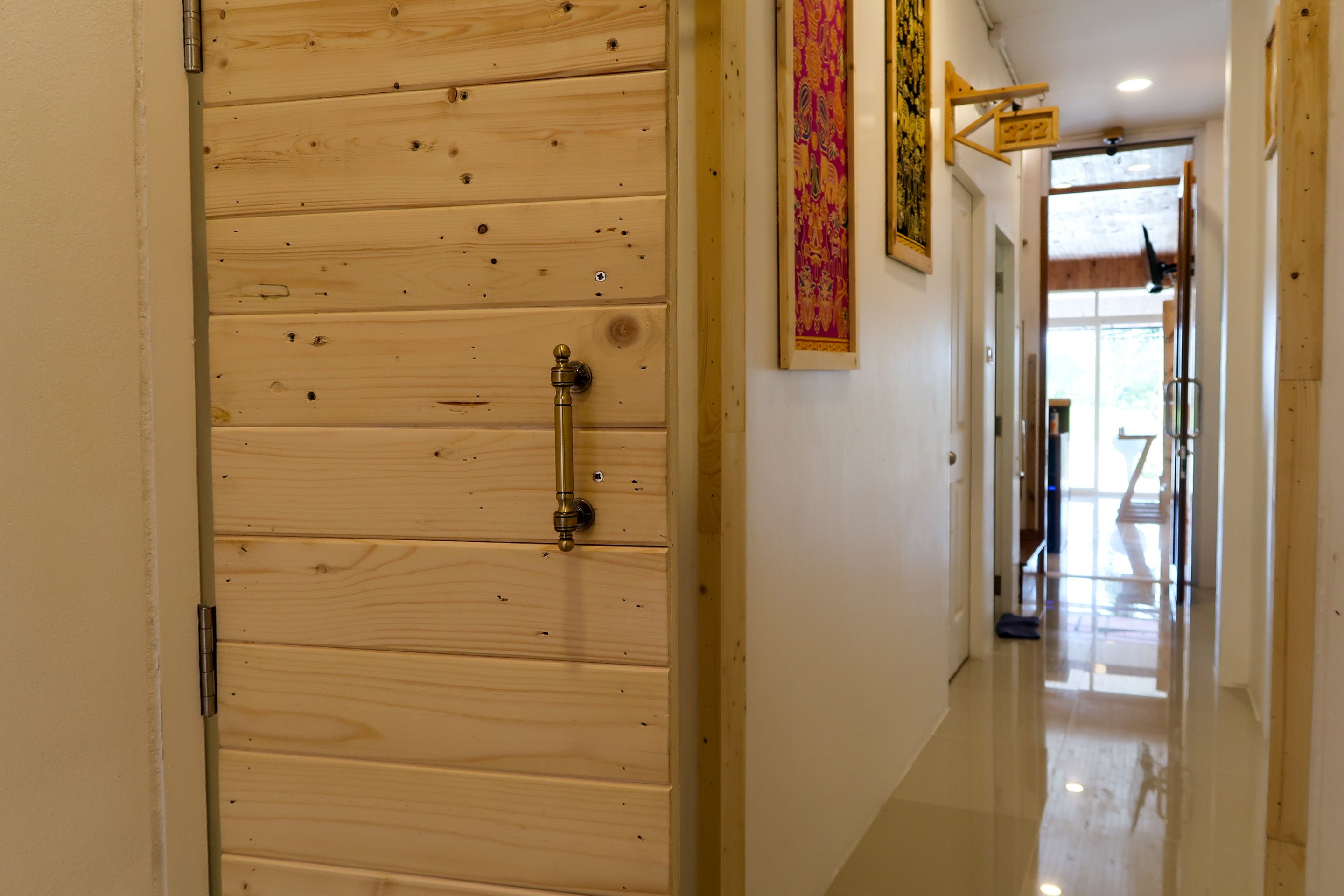 Una puerta de madera con un tirador de latón, un suelo pulido y un pasillo con techo de madera y un cartel colgando.