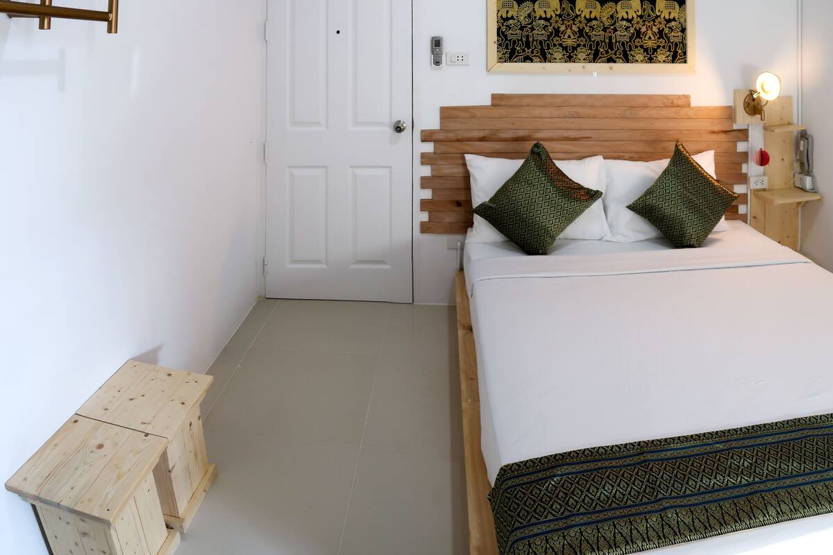 Une chambre à coucher avec une tête de lit en bois, deux coussins à motifs, une porte blanche et un petit tabouret en bois.