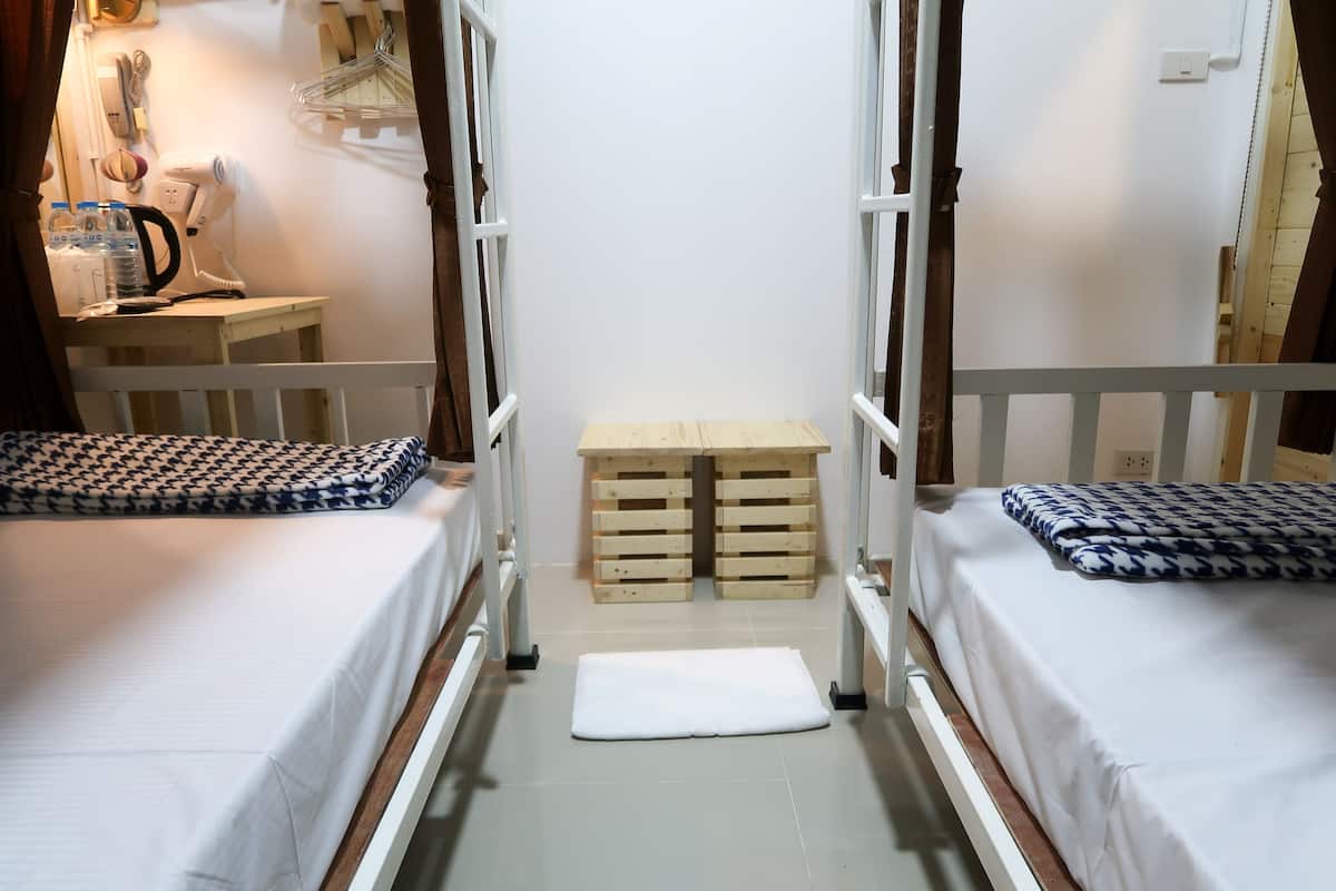 Une chambre avec deux lits, un banc en bois, une table avec un sèche-cheveux et un téléphone fixé au mur.