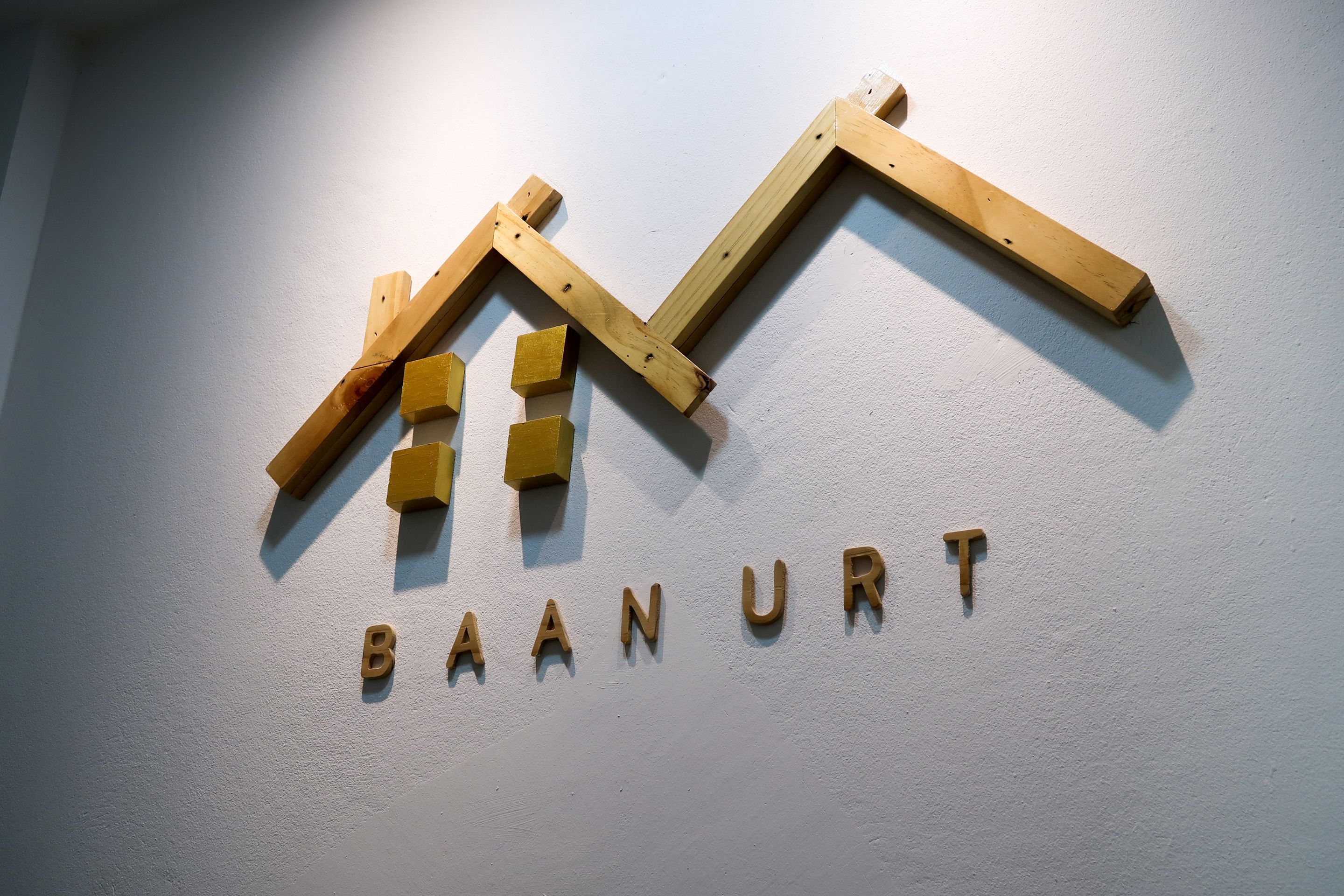 A wooden sign with the text "BAAN URT" on a white wall.