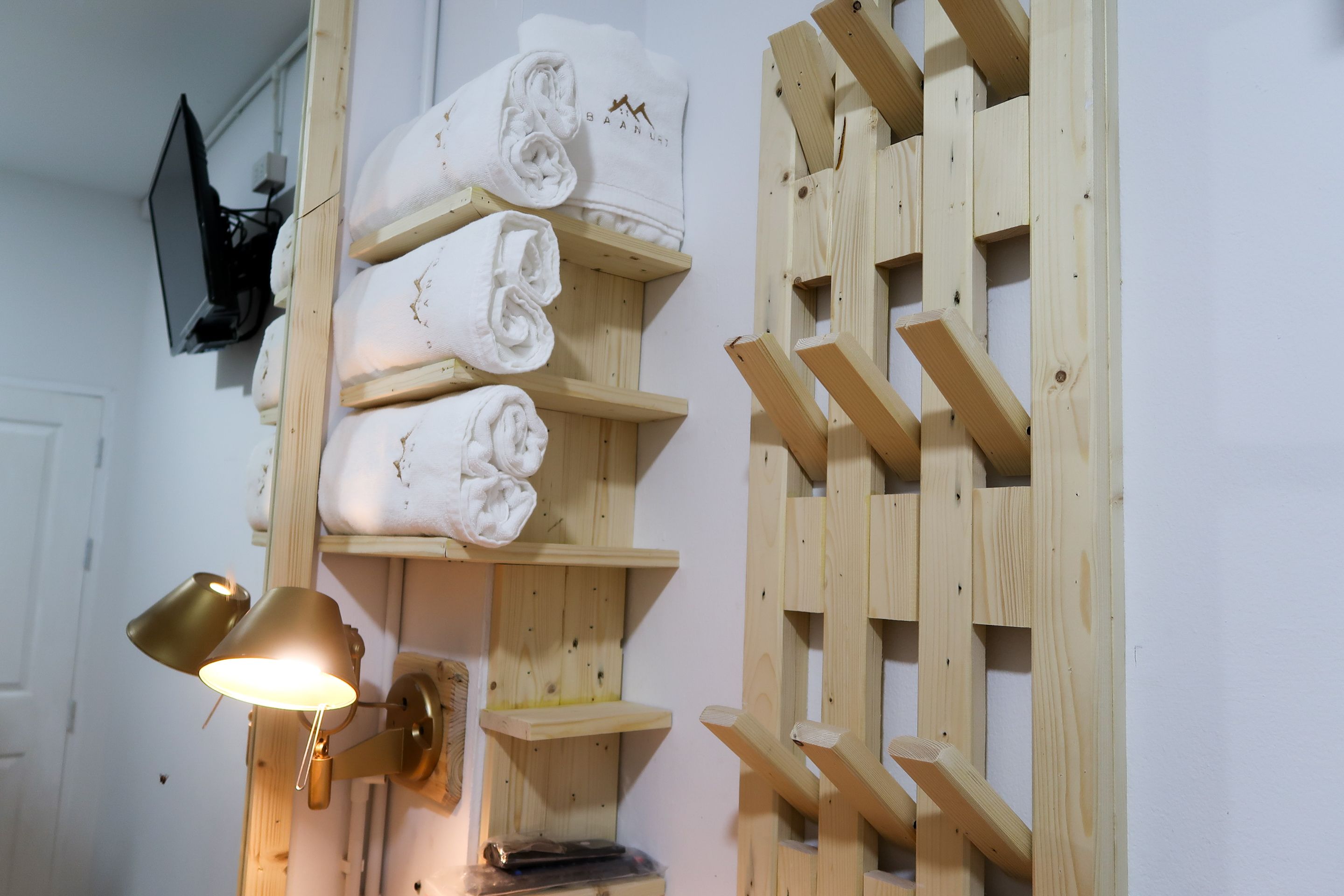 A wooden shelf with neatly folded white towels and a wall-mounted lamp.