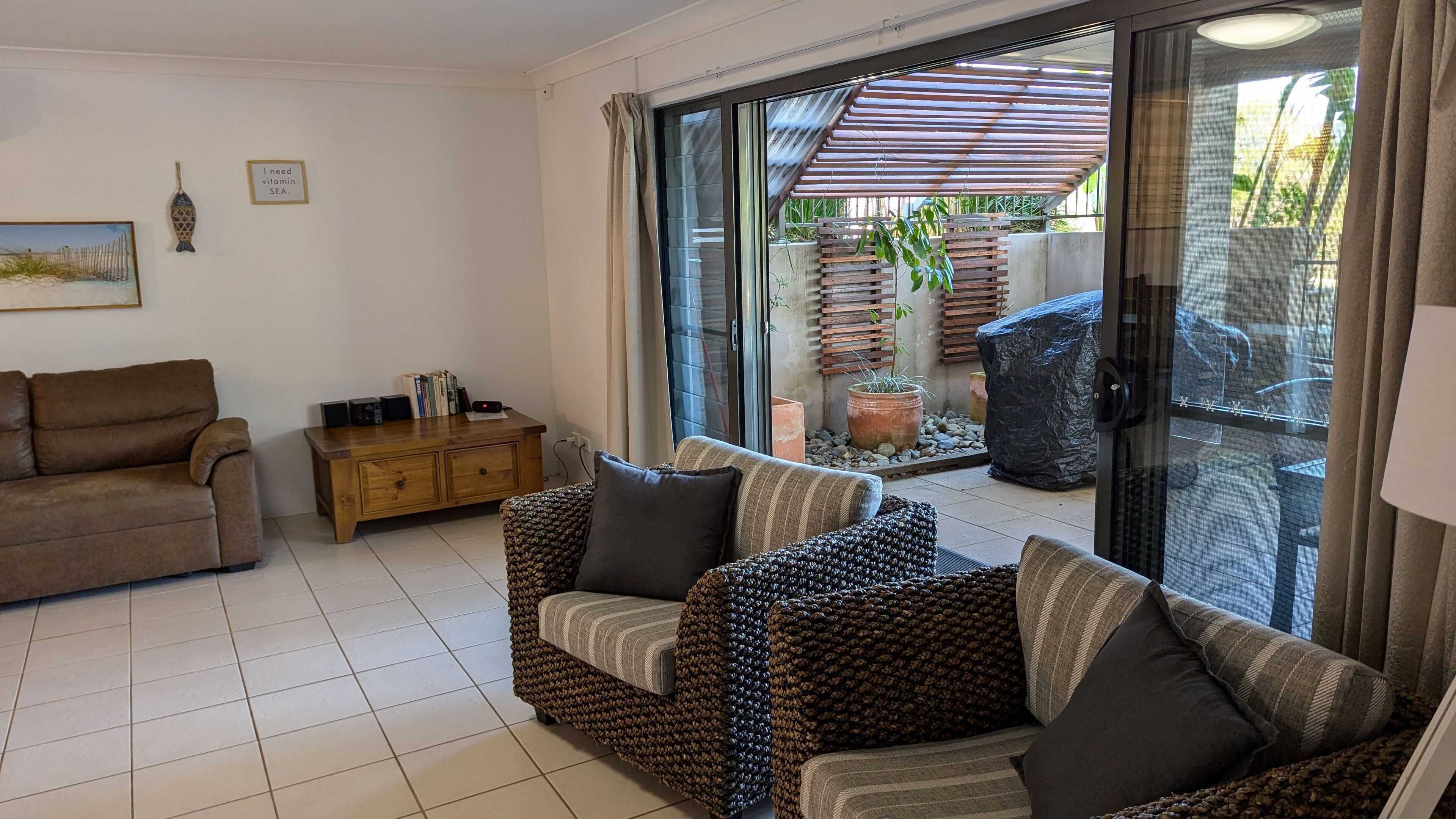 A living room with a sofa, a wooden cabinet, and a sliding glass door leading to an outdoor area with plants and a wooden structure.