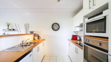 A modern kitchen with white cabinets, stainless steel appliances, and a wooden countertop.
