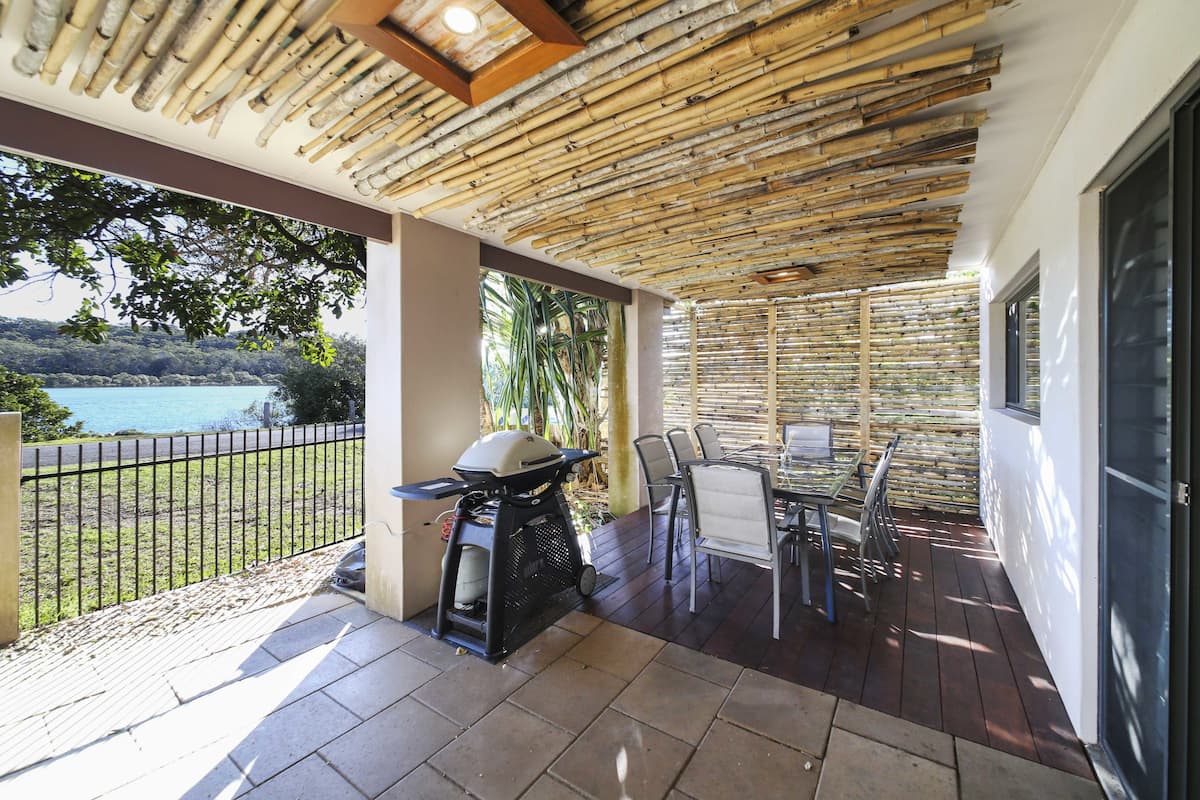 A covered outdoor area with a grill, chairs, and a view of a body of water.
