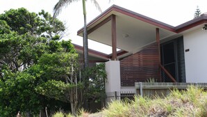 Una casa moderna con un porche cubierto, rodeada de exuberante vegetación y una palmera.