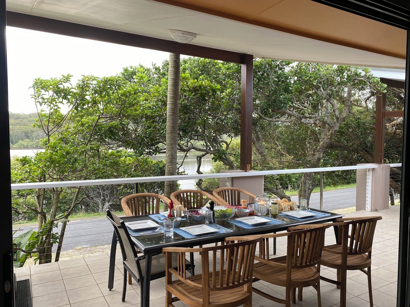 A dining area with a table set for four, surrounded by wooden chairs, overlooking a scenic view of trees and a body of water.