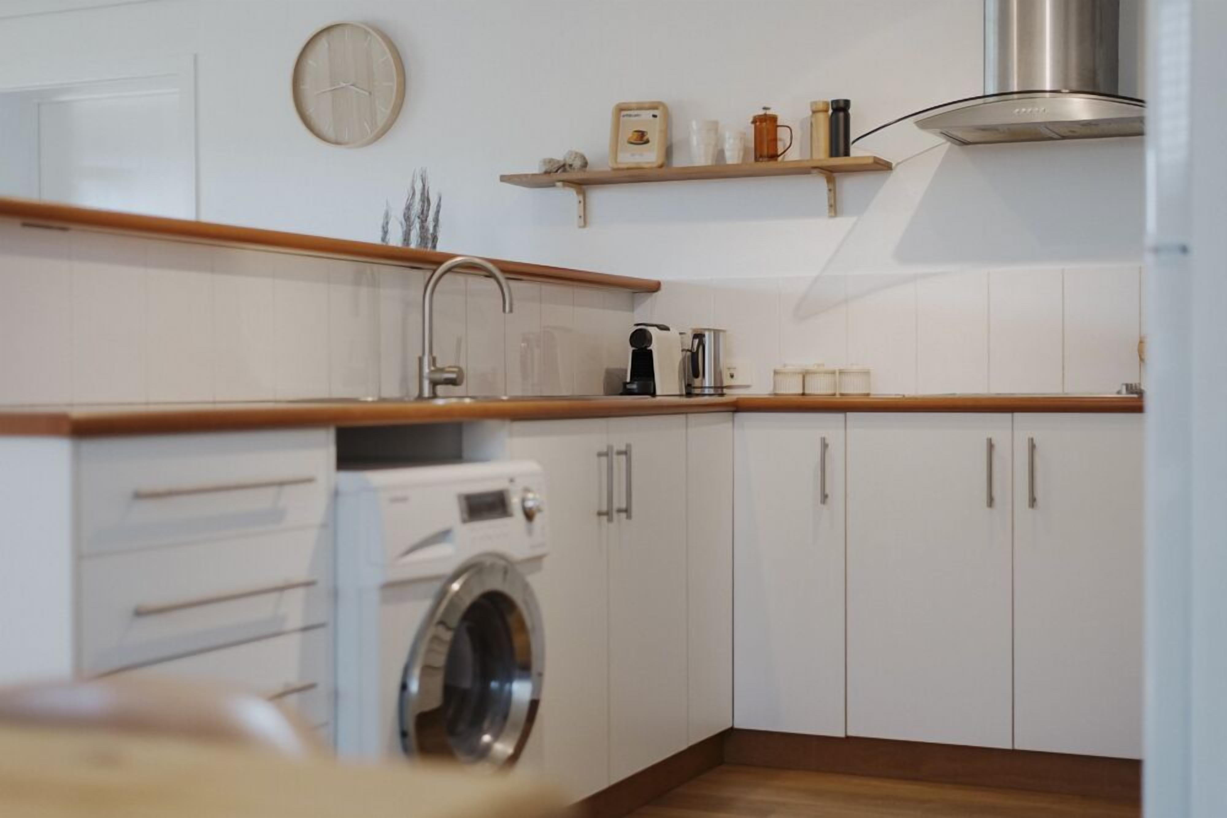 A modern kitchen with white cabinets, a built-in washing machine, wooden countertops, and a stainless steel range hood.